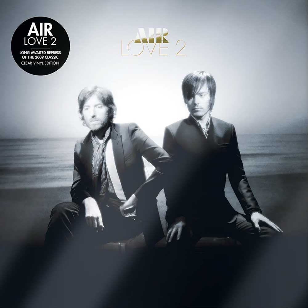 Air - Love 2 (Vinyl 2LP Clear Limited Edition) Air Love 2 vinyl record cover art featuring two men in suits seated against a misty outdoor background, with the title 'AIR LOVE 2' at the top and a black 'AIR LOVE 2' sticker on the upper left.