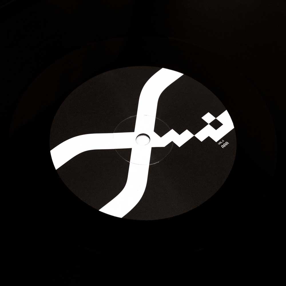 Alva Noto - Xerrox Vol. 1 (Vinyl 2LP) A vinyl record label with a minimalist white geometric Xerrox Vol. 1 logo on a black disc, photographed against a dark background.
