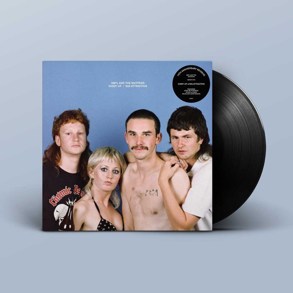 Amyl and The Sniffers - Giddy Up / Big Attraction (10 Year Anniversary) Vinyl LP A vinyl record album shown standing upright with part of the black record visible behind the sleeve. The sleeve features a blue background and Amyl and The Sniffers, with a black circular sticker on the top right.