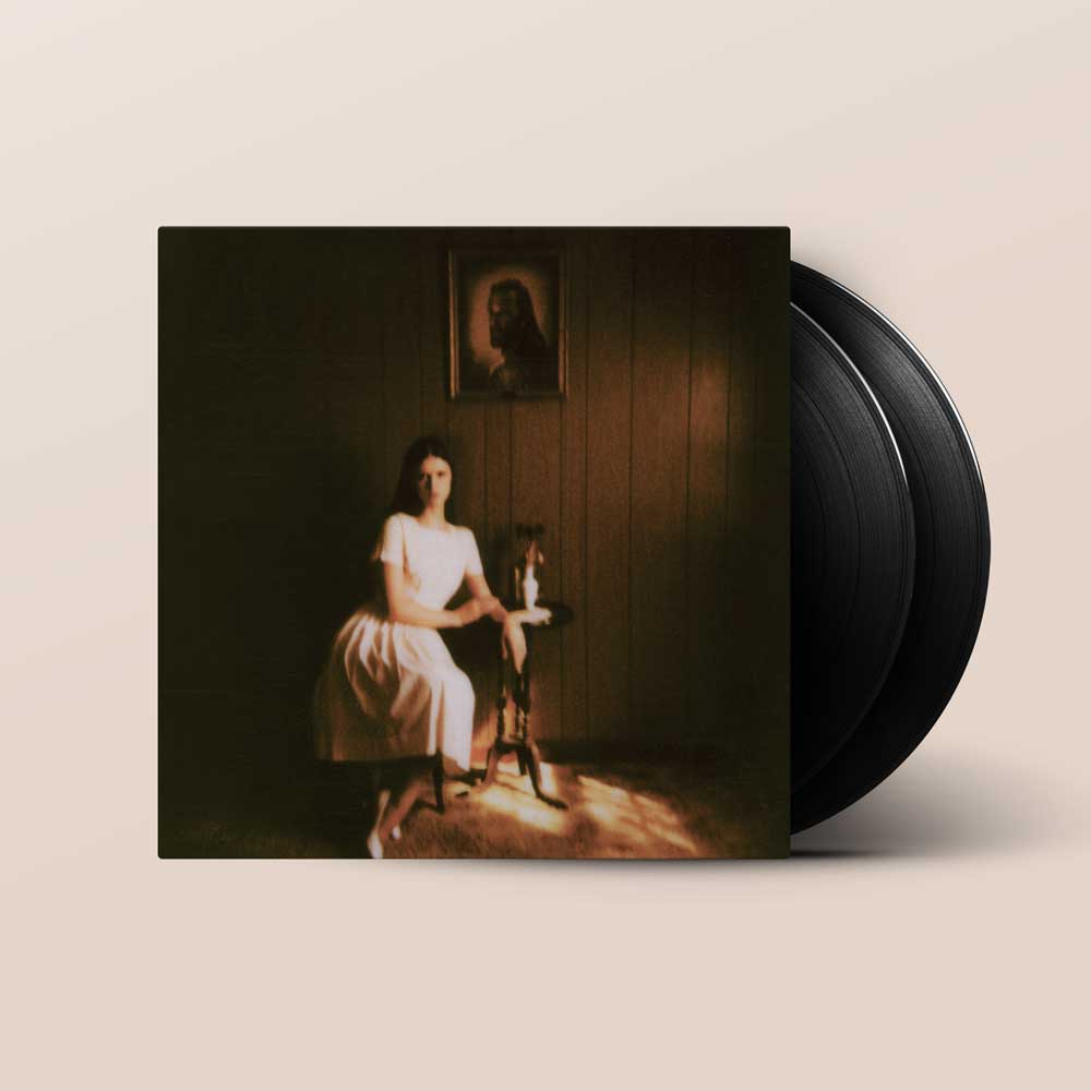 Ethel Cain - Preacher's Daughter (Vinyl 2LP) A vinyl record album with a dark cover photo of a seated woman in a white dress in a dimly lit room, shown with two black records partially visible behind the sleeve on a light beige background.