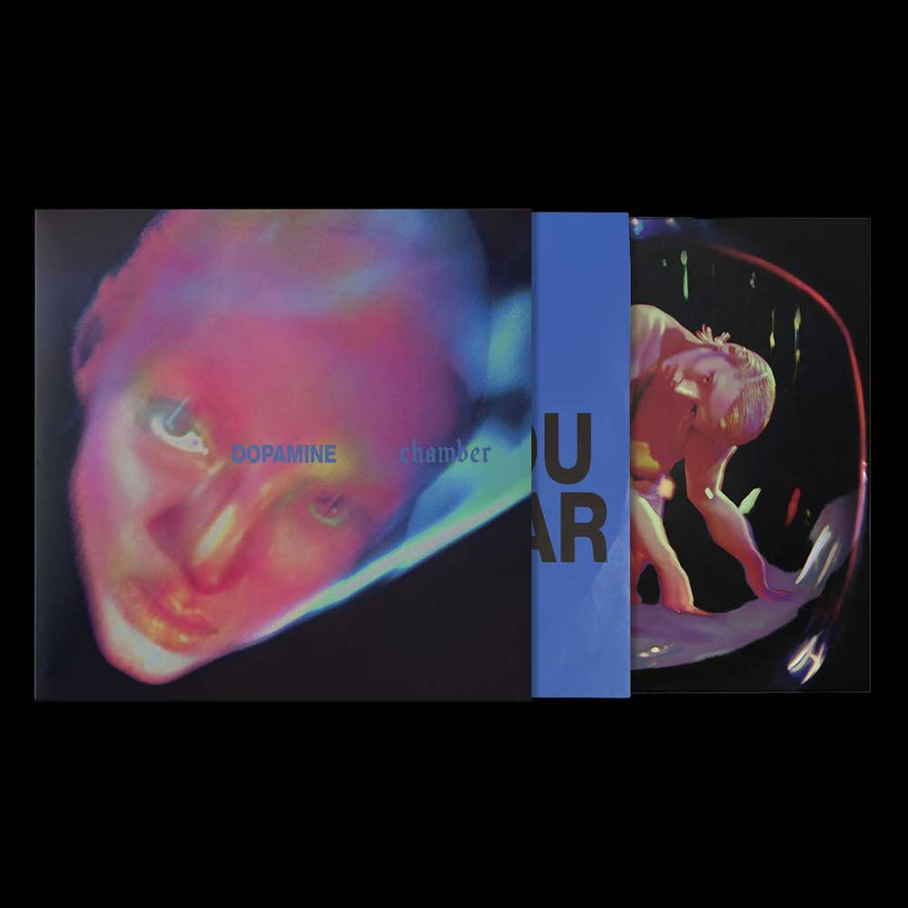 Fontaines D.C. - Dopamine Chamber (Vinyl LP Blue Marble) A album cover with the sleeves slidign out showing a close-up face in pink and blue tones on the left, a blue vertical band with partial white text in the center, and a mirrored figure in a black circular frame on the right.