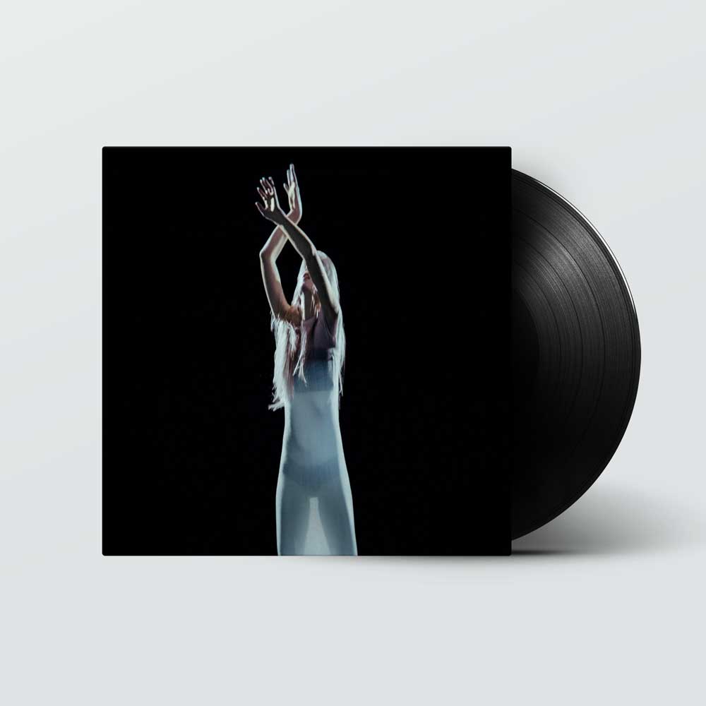 Kelly Moran - Don't Trust Mirrors (Vinyl LP) A vinyl record partially pulled from its sleeve, shown on a light gray background. The album cover features a high-contrast black-and-white photo of a woman in a long white dress with her arms raised, and the record itself is black.