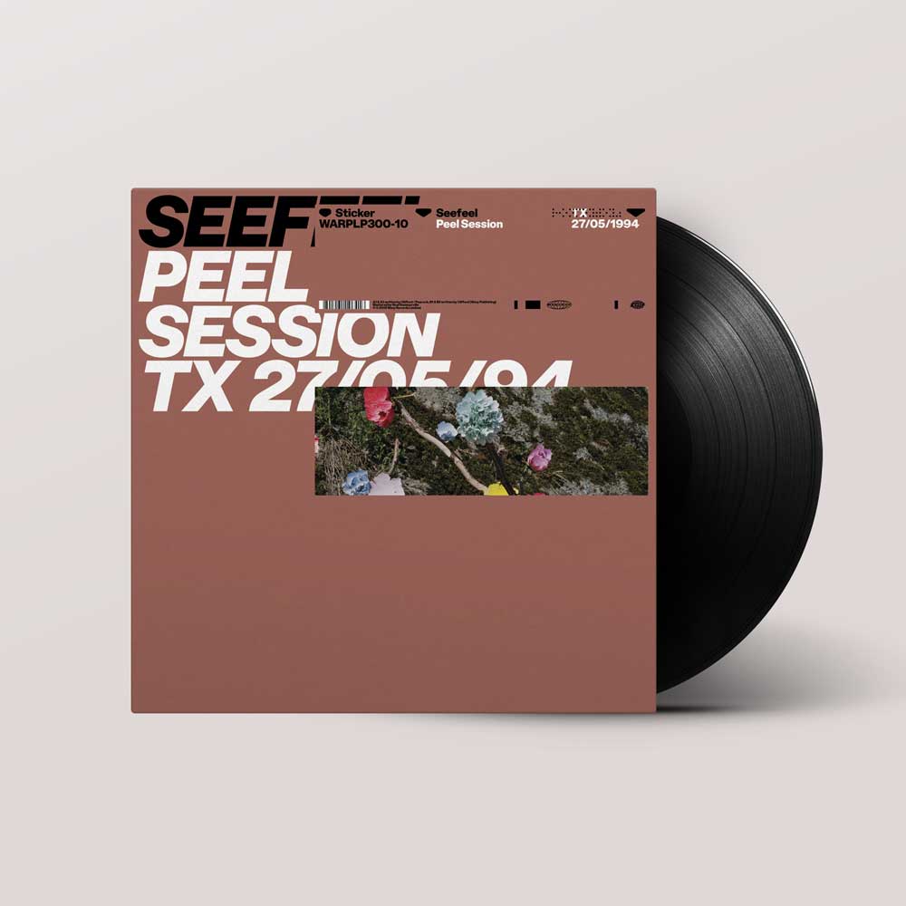 Seefeel - Peel Session (Vinyl 12" EP) A vinyl record partially pulled from its sleeve, shown on a light warm-gray background. The sleeve is dusty rose with bold white text reading 'PEEL SESSION TX 27/05/94' and black text reading 'SEE.