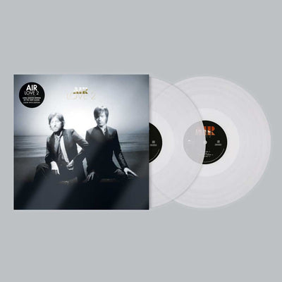 Air - Love 2 (Vinyl 2LP Clear Limited Edition) A vinyl record album shown with its outer sleeve and two clear vinyl records on a plain light gray background. The sleeve features a black-and-white photo of two seated men, with gold 'Love 2' text and a black circular 'Air Quality' label.