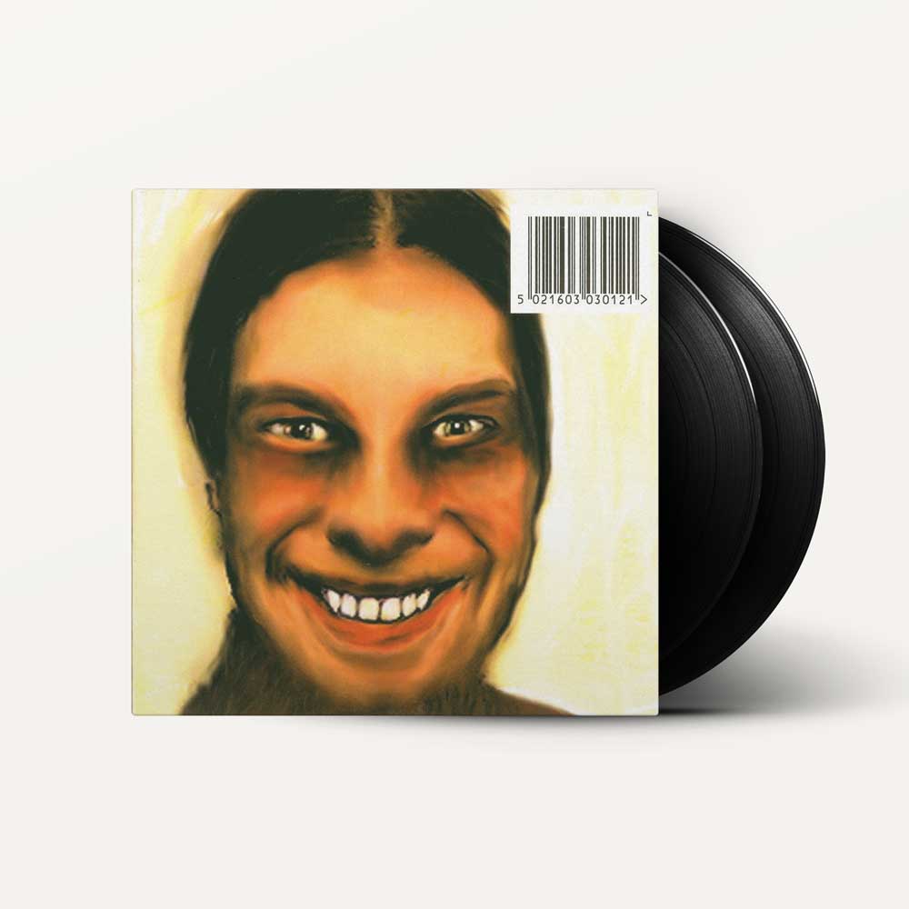 Aphex Twin - ...I Care Because You Do (Vinyl 2LP) A vinyl record album with a square illustrated cover showing a smiling face and a barcode, with two black records partially visible behind the sleeve on a light gray background.