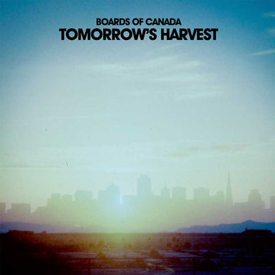 Vinyl Album cover for Boards of Canada's 'Tomorrow's Harvest', featuring a hazy city skyline at sunrise or sunset with a bright sun flare near the horizon and a pale blue sky.