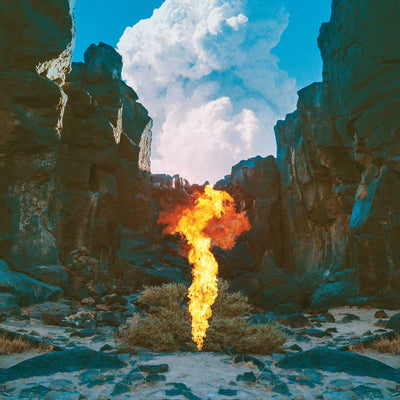 Bonobo - Migration (Vinyl LP 180g) record cover showing a flame rising from a rocky landscape under a blue sky with clouds.