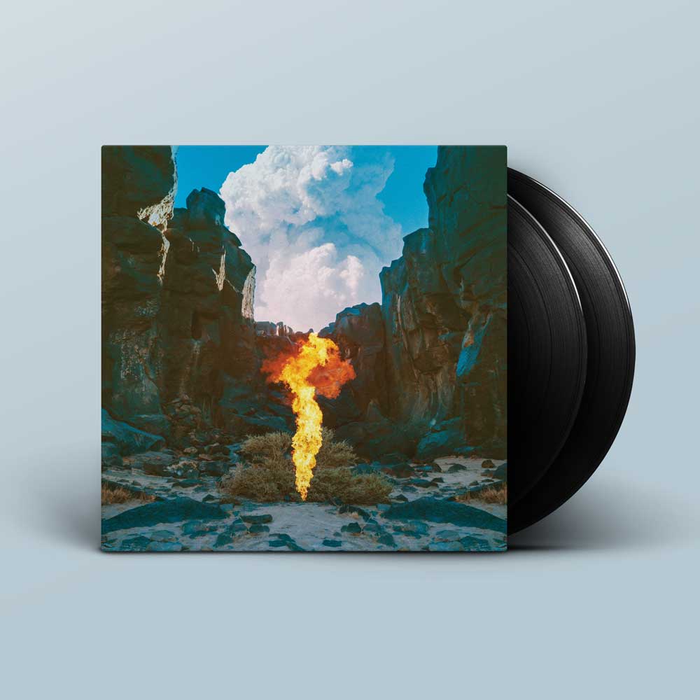 Bonobo - Migration (Vinyl LP 180g) A vinyl record partially pulled from its sleeve, showing the album cover art of a canyon landscape with a bright yellow-orange flame in the centre, set against a light blue-grey background.