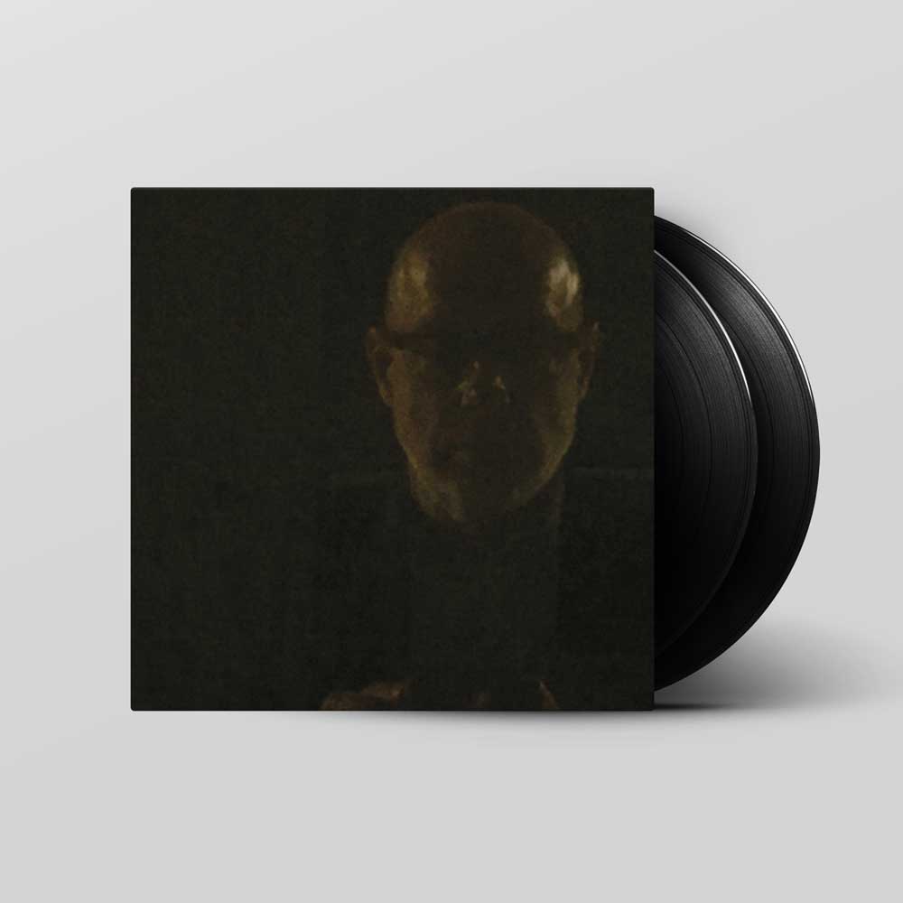 Brian Eno - Reflection (Vinyl 2LP) A vinyl record partially pulled from its sleeve, showing the black record and a dark cover art featuring a dimly lit bald face, set against a light gray background.