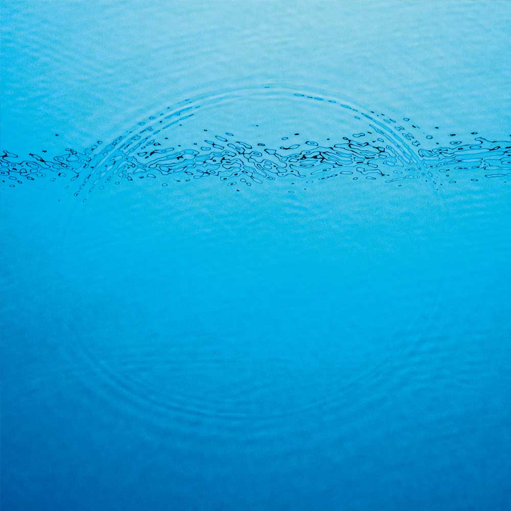 Caribou - Suddenly (Vinyl LP) A close-up photograph of bright blue water with a ripple pattern created by a drop falling on the surface.
