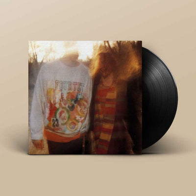 Four Tet - Pause (Vinyl LP 180g) A vinyl record partially pulled from its sleeve, showing the album cover art with a warm-toned photo of two people and a black record disc behind it, set against a plain beige background.