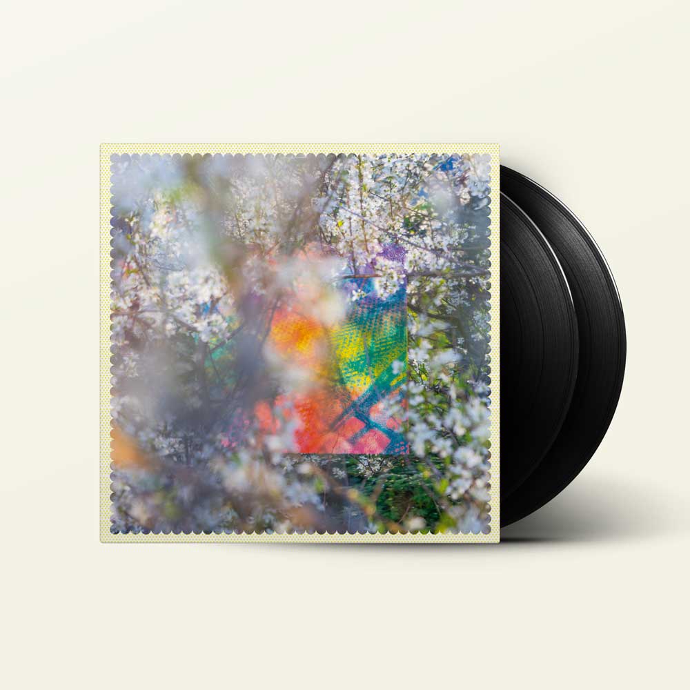 Four Tet - Sixteen Oceans (Vinyl 2LP) A vinyl record partially pulled from its sleeve, showing a colorful abstract floral artwork with white blossoms and a rainbow-like center, alongside a black record on a light cream background.