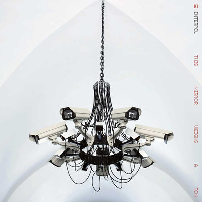 Interpol - This Mirror Weighs a Ton (Vinyl 2LP Transparent Red) Vinyl record album cover showing a multi-camera ceiling chandelier featuring numerous white security cameras with black lenses and numerous black cables, suspended from a black chain against a white arched ceiling.