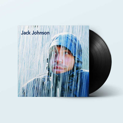 Jack Johnson – Brushfire Fairytales (High Def Edition) A vinyl record partially pulled from its sleeve, showing the album cover art for Jack Johnson. The cover features a man in a blue raincoat looking out in the rain, with the black vinyl disc visible behind the sleeve on a light blue background.